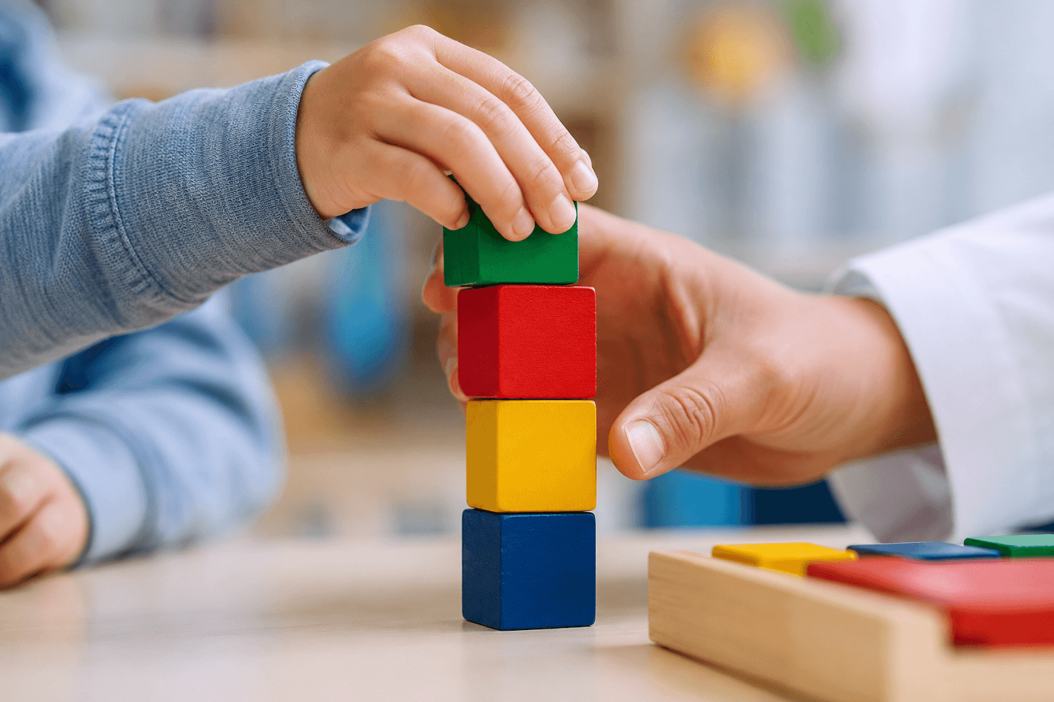 Kind stapelt bunte Holzbausteine gemeinsam mit einer Ergotherapeutin